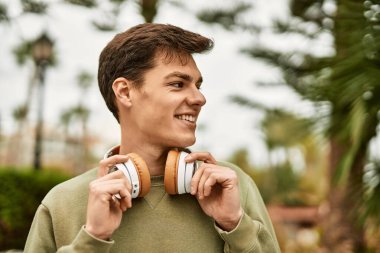 Şehirde kulaklık takarak mutlu gülümseyen genç İspanyol adam..