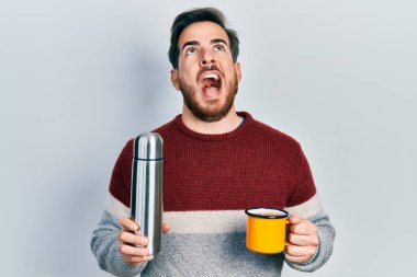 Sakallı yakışıklı beyaz adam bir fincan kahve içiyor. Elinde termo var. Kızgın ve kızgın çığlıklar atıyor, öfkeyle bağırıyor.. 