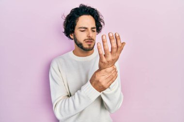 Yakışıklı, beyaz süveter giyen, elleri ve parmakları ağrıyan, eklem iltihabı olan İspanyol bir adam. 