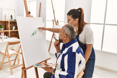 Genç resim öğretmeni kadın sanat stüdyosundaki tuvalde resim yapan yaşlı adama resim öğretiyor.