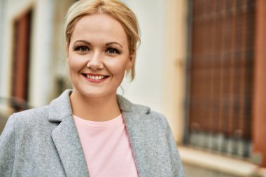 Genç sarışın iş kadını gülümseyerek şehirde mutlu mesut duruyor..