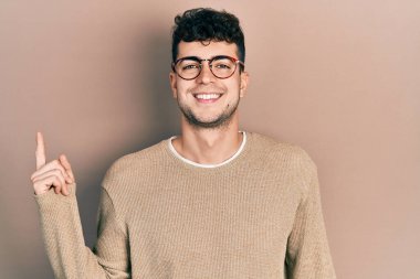 Gündelik kıyafetler ve gözlük takan, yüzünde kocaman bir gülümseme olan genç İspanyol adam kameraya el ile işaret ediyor.. 