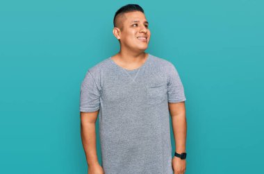 Gündelik kıyafetler giyen genç latin adam yüzünde gülümsemeyle yan yana bakıyor, doğal bir ifade. Kendinden emin gülen. 