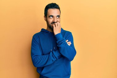 Günlük kıyafetler giyen genç İspanyol adam gergin ve gergin görünüyor. Ağzı tırnak yiyen eller. anksiyete. 