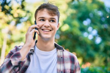 Genç beyaz adam gülümsüyor. Şehirdeki akıllı telefondan konuşuyor..