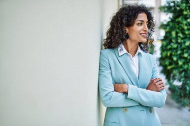 Profesyonel giyinen genç İspanyol iş kadını. Şehre gülümsüyor. Duvara yaslanıyor.