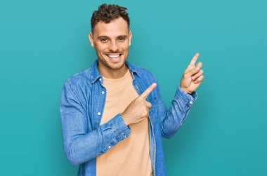 Gündelik kıyafetler giyen genç İspanyol adam gülümseyip kameraya bakıyor ve iki eliyle ve parmaklarıyla kenarı işaret ediyor.. 