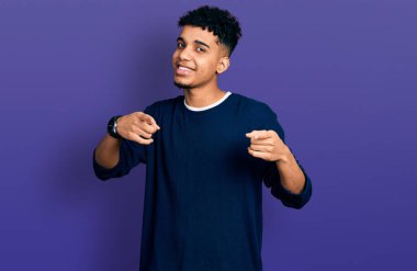 Sıradan kıyafetler giymiş genç Afro-Amerikalı adam mutlu ve komik yüzüyle kamerayı işaret ediyor. iyi enerji ve titreşimler. 