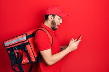 Sırt çantası taşıyan İspanyol bir adam akıllı telefon kullanıyor. Şaşırmış ve şaşırmış bir ifade, korku ve heyecanlı bir yüz ifadesi var.. 