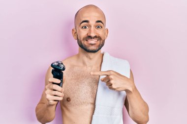 Genç kel adam elinde jilet tutarken mutlu bir şekilde el ve parmağıyla işaret ediyor. 