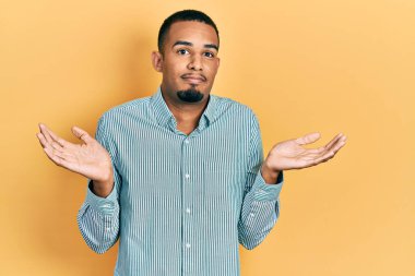 Sıradan kıyafetler giyen, kafası karışmış, elleri ve kolları havada genç Afro-Amerikalı bir adam. şüphe kavramı. 