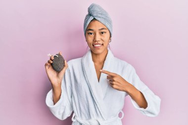 Duş havlusu şapkası ve bornoz giyen genç Çinli kadın elinde sünger taşı tutarken mutlu bir şekilde elini ve parmağını gösterdi. 