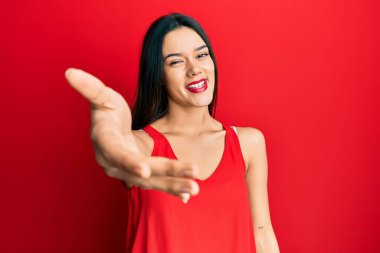 Kolsuz tişörtlü, sıradan giyinen genç İspanyol kız dostça bir selamlama ve hoş geldin hediyesi olarak gülümsüyor. başarılı iş. 