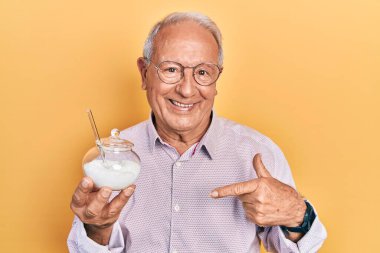 Yaşlı adam elinde şeker dolu kaseyle mutlu ve gururlu gülümseyen birini işaret ediyor. 