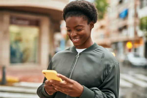 若いアフリカ系アメリカ人の女の子が市内でスマートフォンを使って笑顔で — ストック写真