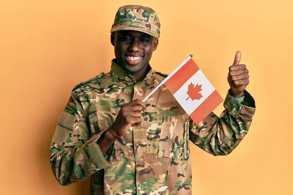 身穿军服的年轻的非洲裔美国人 高高兴兴地举着加拿大国旗 竖起大拇指 做得出色 签了字 — 图库照片