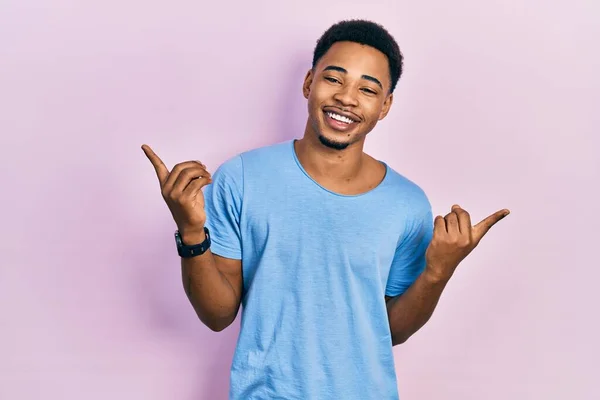 カジュアルなブルーのTシャツを着た若いアフリカ系アメリカ人男性は さまざまな方向に指で自信を持って指して笑っています 広告のコピースペース — ストック写真