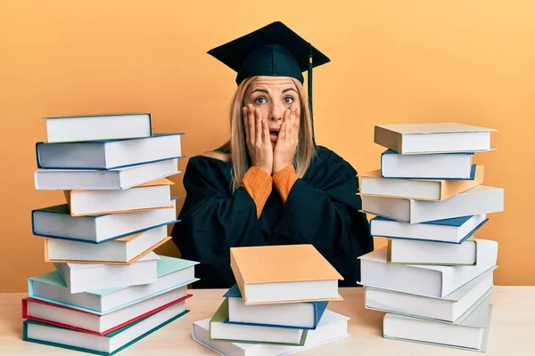 Young Caucasian Woman Wearing Graduation Ceremony Robe Sitting Table Afraid — Stock Photo, Image