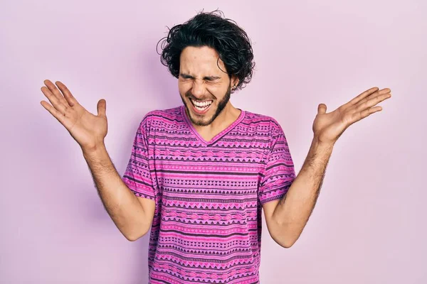 腕を上げて成功のために狂気と狂気を祝うカジュアルなピンクのTシャツを着てハンサムなヒスパニック系の男と興奮叫んで目を閉じた 勝者のコンセプト — ストック写真