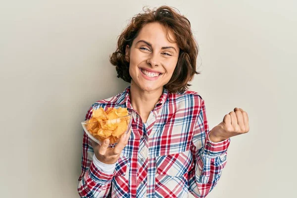 Young Brunette Woman Holding Potato Chips Screaming Proud Celebrating Victory — Stock Photo, Image