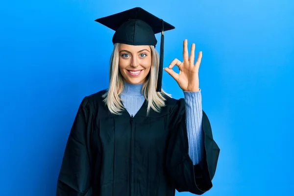 卒業キャップと式のローブを身に着けている美しいブロンドの女性は 手や指でOkサインを行う積極的な笑顔 成功した表現 — ストック写真