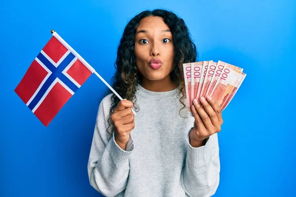 年轻的拉丁女子举着诺威国旗和挪威克朗钞票 看着摄像机 飞吻着可爱而性感 爱的表达 — 图库照片