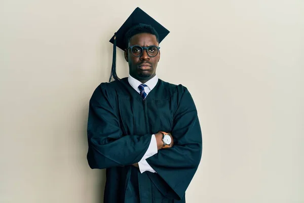 Handsome black man wearing graduation cap and ceremony robe skeptic and nervous, disapproving expression on face with crossed arms. negative person.