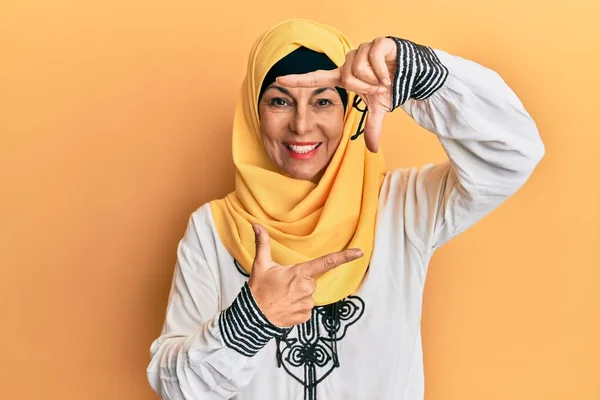 伝統的なイスラムのヒジャーブスカーフを身に着けている中世のヒスパニック女性は 幸せな顔で手や指でフレームを作り笑顔 創造性と写真の概念 — ストック写真