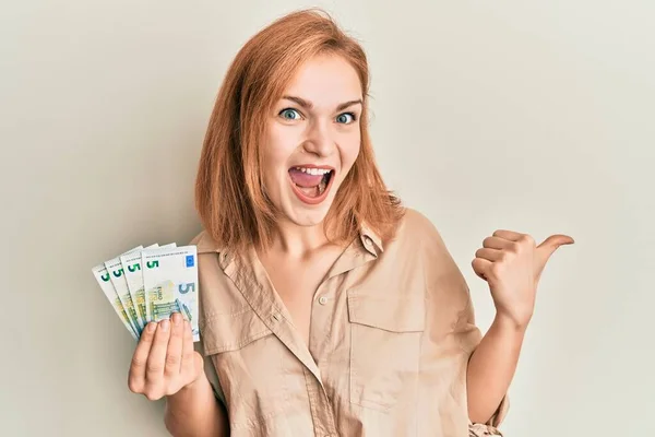 Young Caucasian Woman Holding Bunch Euro Banknotes Pointing Thumb Side — 图库照片