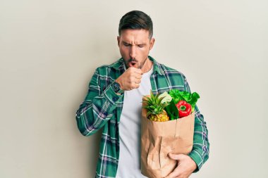 Sakallı yakışıklı bir adam elinde poşetle kendini iyi hissetmiyor ve soğuk algınlığı veya bronşitin belirtisi olarak öksürüyor. sağlık hizmeti kavramı. 