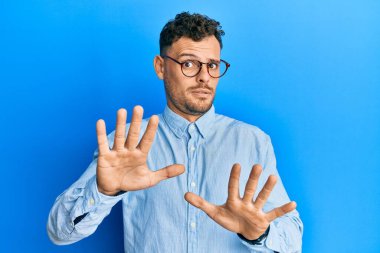 Gündelik kıyafetler giyen ve gözlük takan genç İspanyol bir adam. Avuçlarını hareket ettiriyor. Korkmuş ve iğrenç bir ifadeyle reddediyor. Dur ve yasakla. 