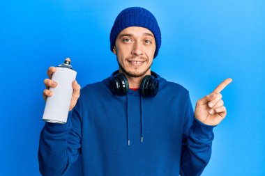 Süveter giyen İspanyol genç adam, elinde grafiti spreyi ile gülümsüyor. 