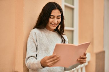 Genç ortadoğu öğrencisi kız şehirde mutlu bir şekilde kitap okuyor..