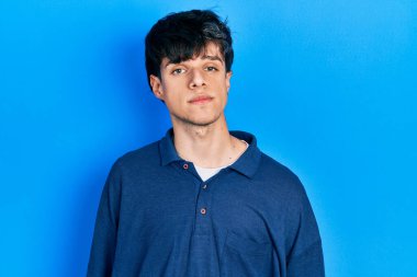 Yüzünde ciddi bir ifadeyle mavi arka planda mahsur kalmış yakışıklı hippi genç adam. Basit ve doğal bir şekilde kameraya bakıyorsun.. 