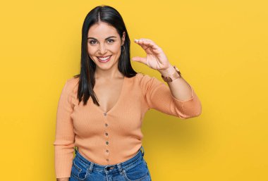 Gündelik kıyafetler giyen, gülümseyen, kendine güvenen, el hareketi yapan, parmaklarıyla işaret yapan ve kameraya bakan genç İspanyol kadın. ölçüm kavramı. 