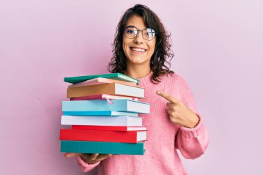 Bir yığın kitap tutan genç İspanyol kadın mutlu bir şekilde el ve parmağıyla işaret ediyor. 