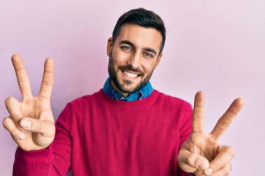 Gündelik giysiler giymiş, ağzı açık gülümseyen genç İspanyol adam zafer işareti yaparken parmaklarını gösteriyor. İki numara.. 