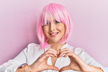 Genç sarışın kadın, pembe peruk takıyor. Aşkla gülümsüyor. Elleriyle kalp sembolü ve şekli gösteriyor. romantik kavram. 