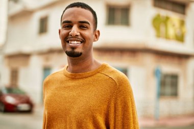 Genç Afrikalı Amerikalı adam gülümseyerek şehirde mutlu mesut duruyor..