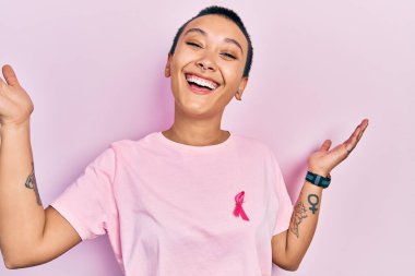 Kısa saçlı güzel İspanyol kadın pembe kanser kurdelesi takmış zaferi mutlu bir gülümsemeyle ve ellerini kaldırarak kazanan ifadeyle kutluyor. 