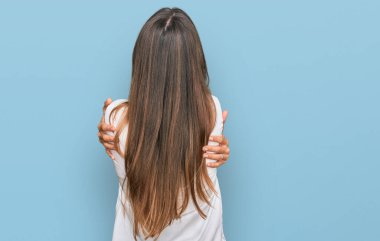 Genç ve güzel bir kadın gündelik giysiler giyip kendine sarılıyor, mutlu ve pozitif bir şekilde. Sevgi ve özgüven. 