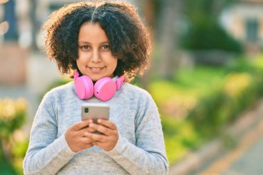 Sevimli İspanyol çocuk parkta akıllı telefon ve kulaklık kullanarak müzik dinliyor..