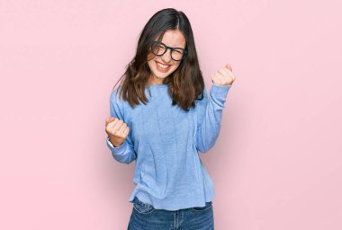 Gündelik kıyafet ve gözlük takan genç ve güzel bir kadın başarıyı kolları havada ve gözleri kapalı kutluyor ve hayrete düşüyor. Kazanan konsept. 