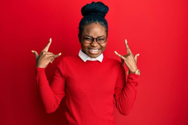 Sıradan kıyafetler ve gözlük takmış, çılgın bir ifadeyle bağıran, elleri havada rock sembolü yapan genç Afrikalı Amerikalı bir kadın. Müzik yıldızı. ağır kavram. 