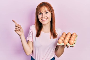 Kızıl saçlı genç kadın gülümseyen taze yumurtalar gösteriyor mutlu bir şekilde elini ve parmağını kenarda gösteriyor. 