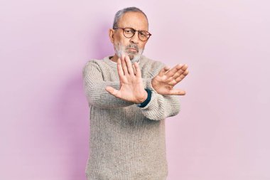 Sakallı, günlük süveter giyen ve gözlük takan yakışıklı bir adam. Kollarını kavuşturup, avuç içlerine negatif işaretler çiziyor. Kızgın bir surat. 