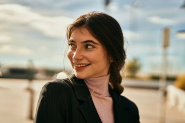 Genç ve güzel bir iş kadını gülümseyerek şehirde mutlu mesut duruyor..