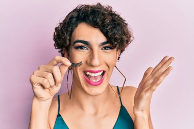 Takma kirpiklerle makyaj yapan genç adam başarıyı mutlu bir gülümsemeyle kutluyor ve kazanan el kaldırarak ifade ediyor. 