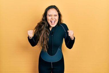 Genç İspanyol kız neoprene üniforması giyiyor kızgın ve kızgın yumruklar sallıyor öfkeyle bağırırken sinirli ve öfkeli. öfke ve agresif konsept. 