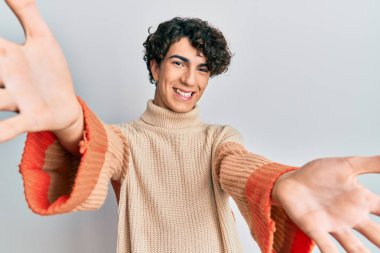 Sıradan bir kazak giyen İspanyol genç adam kameraya sarılmak için gülümseyerek bakıyor. Mutluluğu kucaklayan neşeli bir ifade.. 